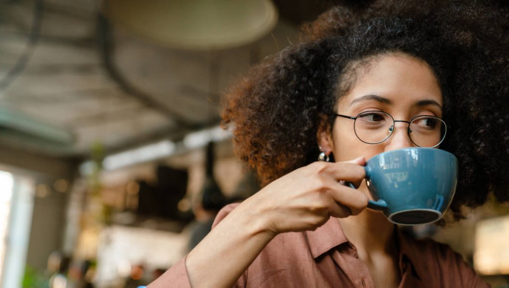 Mujer joven tomando café acompañada de galletita caramelizada Prosalud